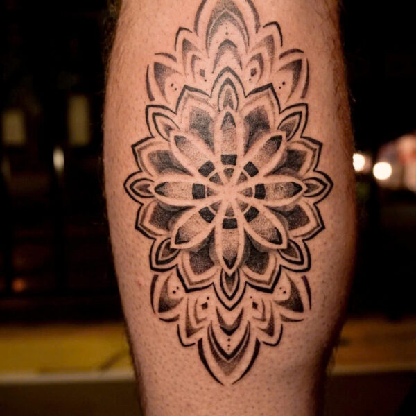 Black and grey dotwork mandala tattooed on the back of a calf
