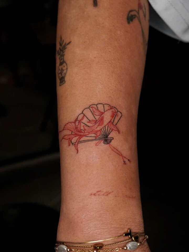 Small red lotus tattoo on the inside of a forearm