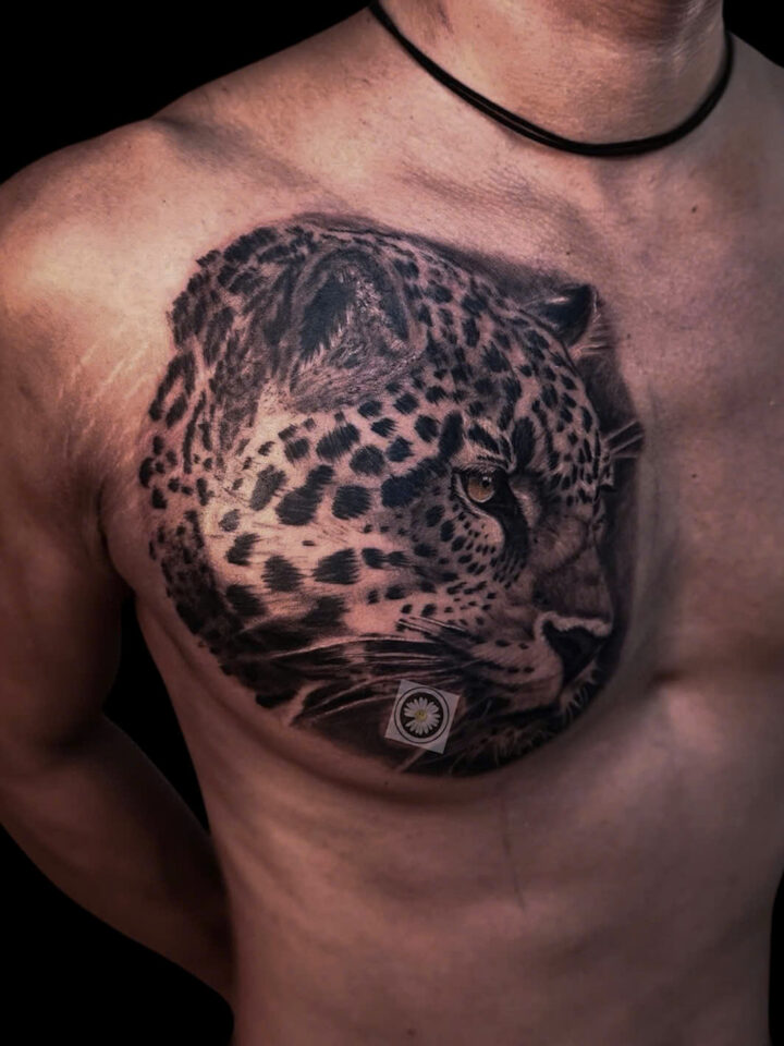 Black and grey leopard portrait tattooed across a chest