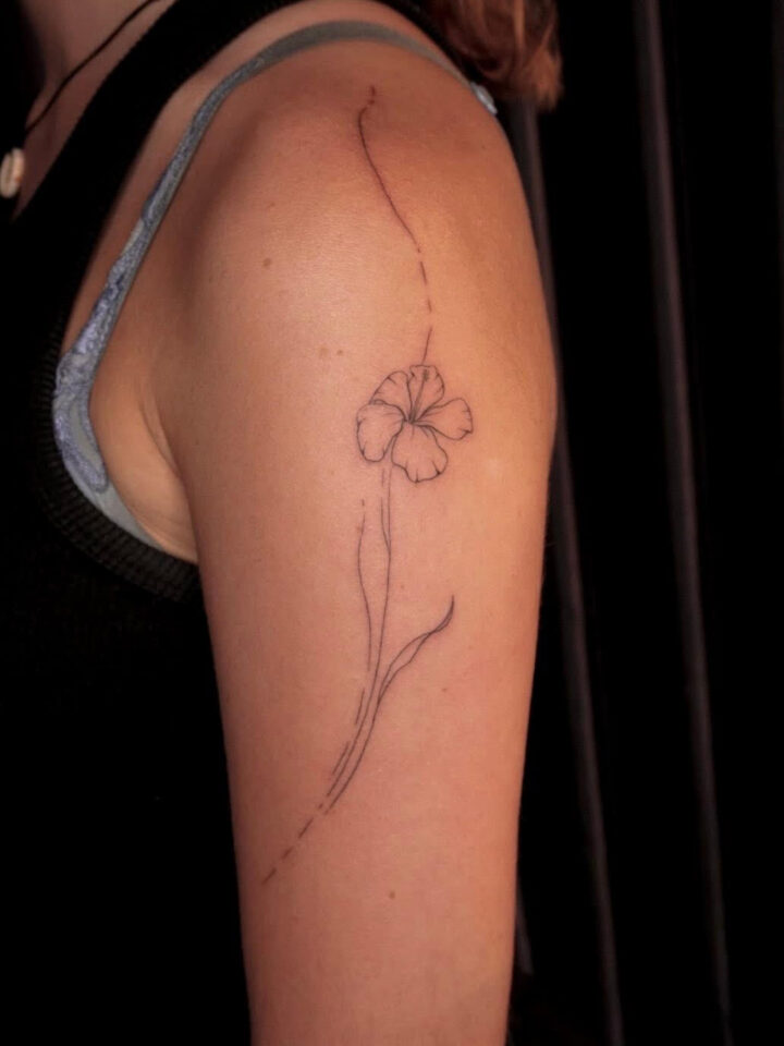 Fine line flower tattooed down an upper arm