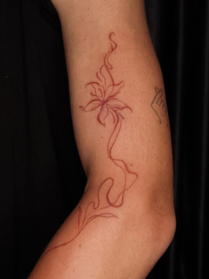 Red fine line floral tattoo running down an arm