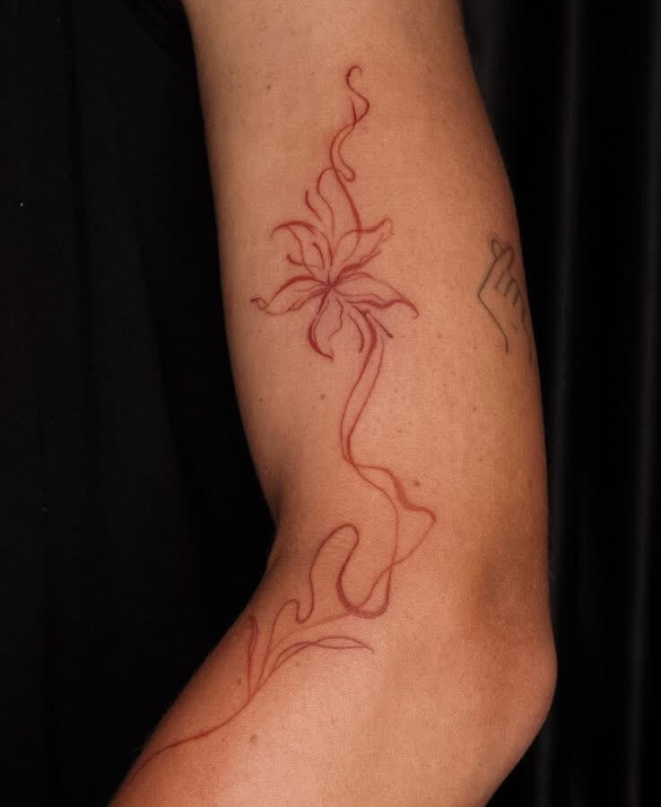 Red fine line floral tattoo running down an arm