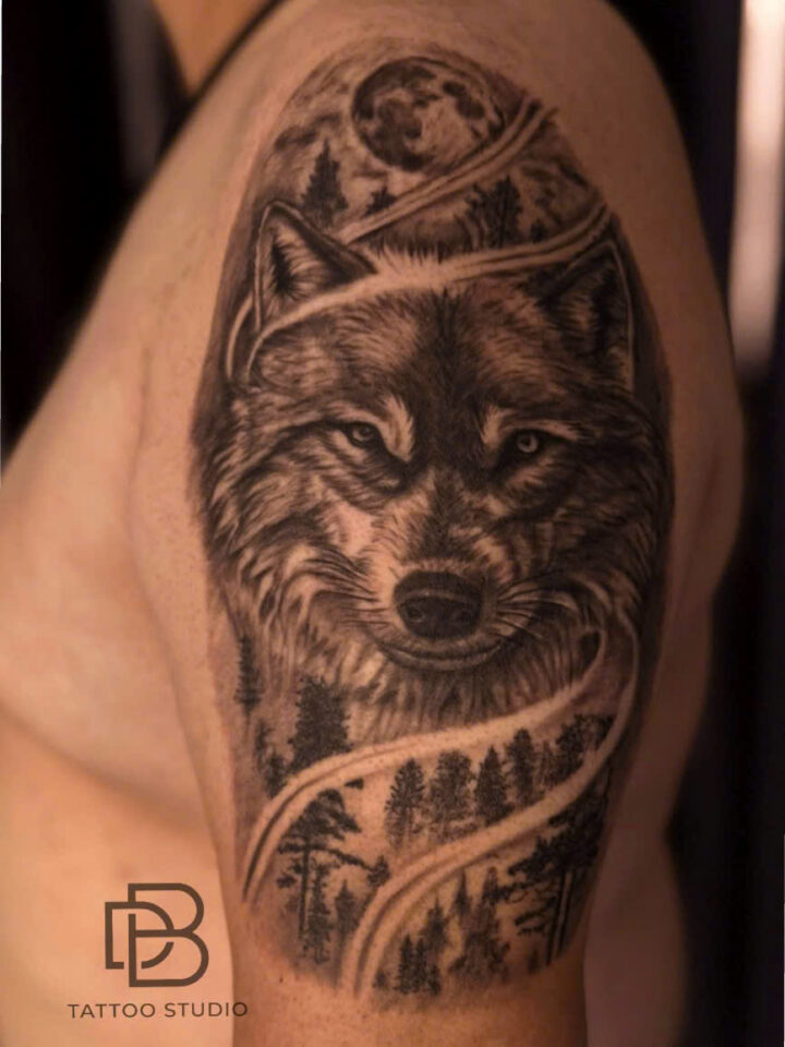 Black and grey wolf and forest tattooed on an upper arm