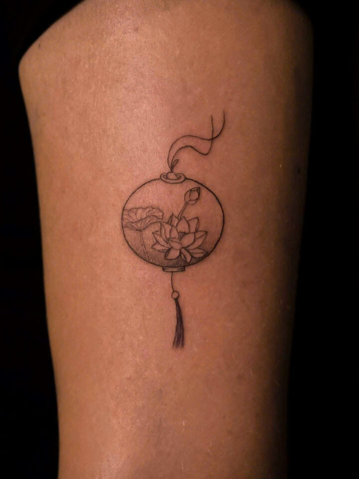Mini lantern and lotus tattoo on the side of a thigh