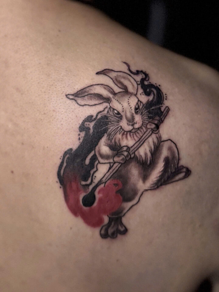 Rabbit warrior with a staff and red flame tattooed on a shoulder blade