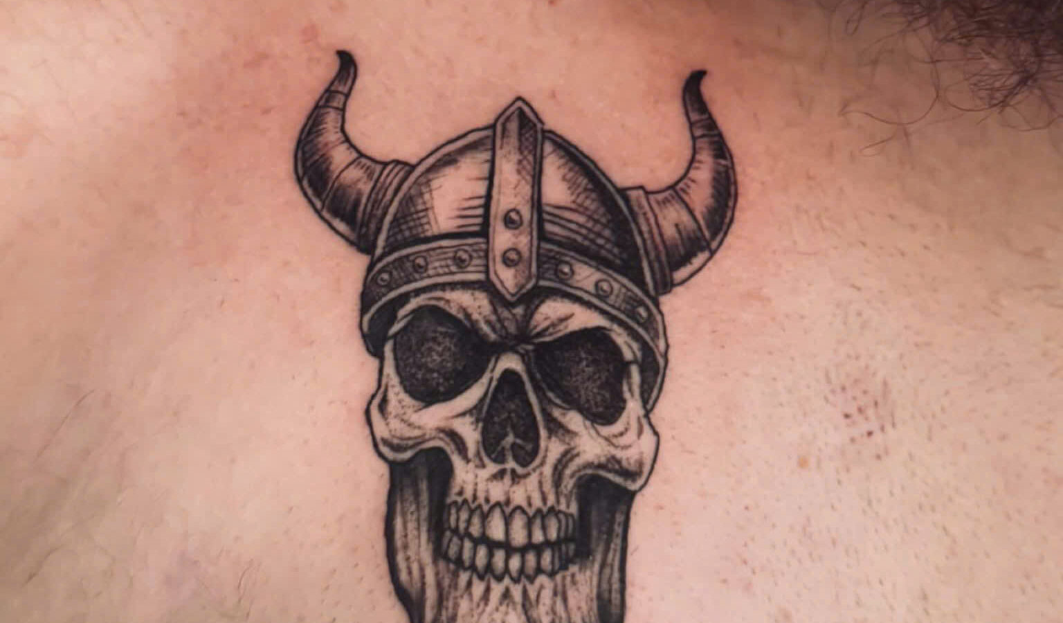 Blackwork viking skull in a horned helmet tattooed on a chest