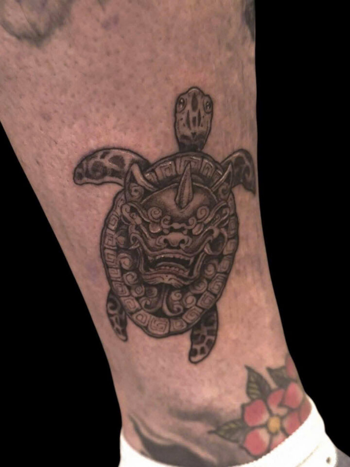 Sea turtle with an ornamental mask on its shell, tattooed on an ankle