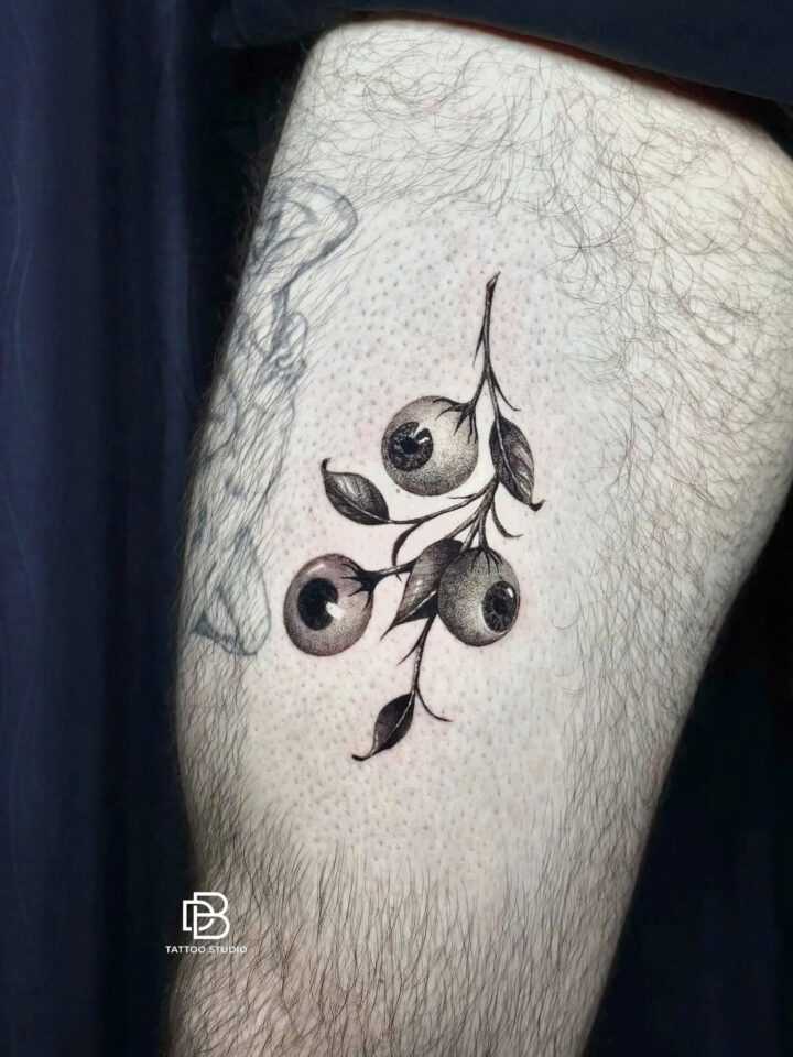 Black and grey blueberry branch tattooed on a thigh