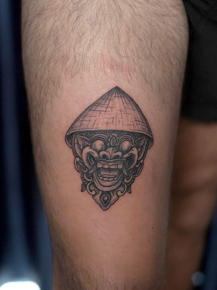 Ornamental guardian mask with a conical crown tattooed on a calf