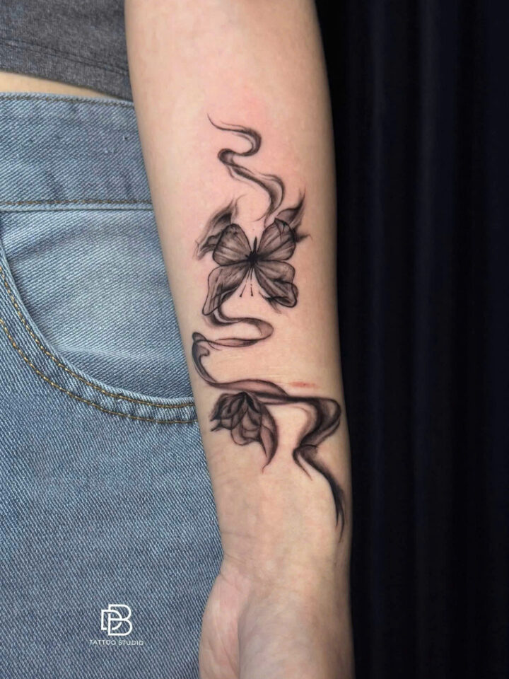 Black and grey butterflies with trailing smoke wrapped around a forearm
