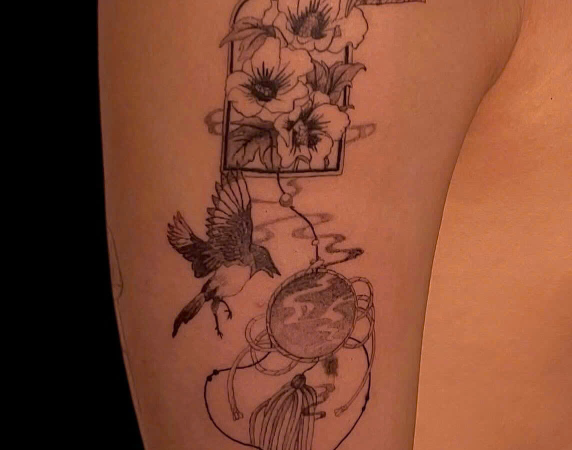 Fine line floral and bird composition tattooed down an upper arm