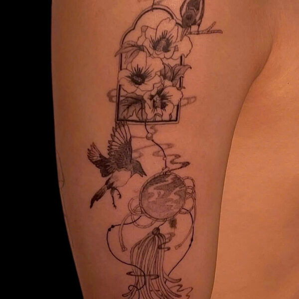 Fine line floral and bird composition tattooed down an upper arm