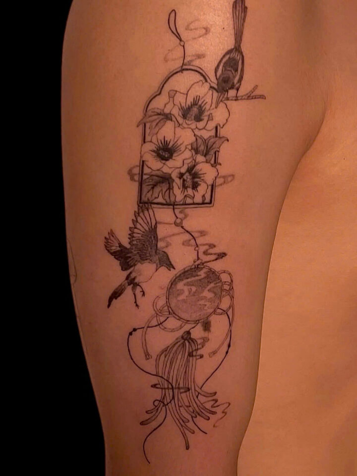 Fine line floral and bird composition tattooed down an upper arm