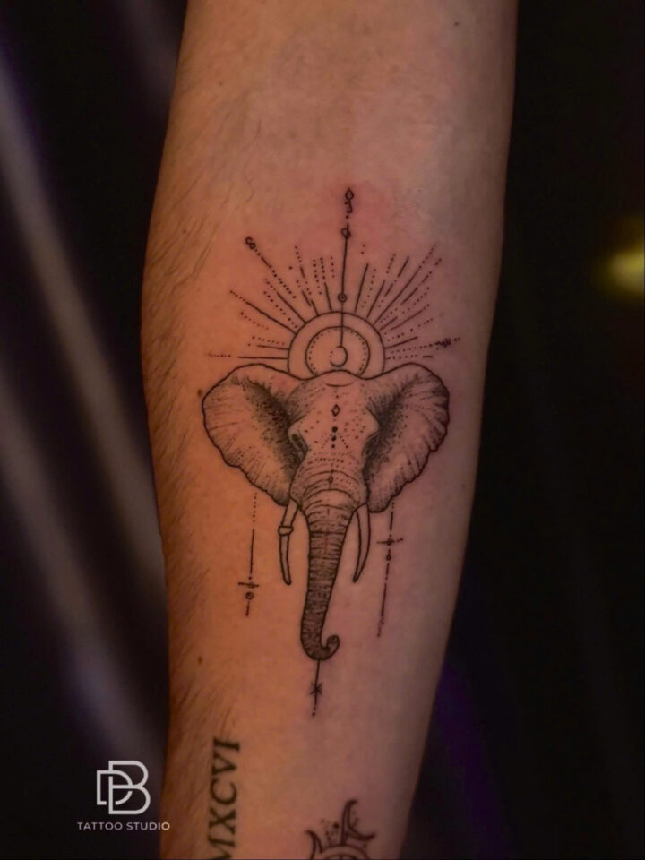 Ornamental elephant head with a sunburst and geometric lines on a forearm