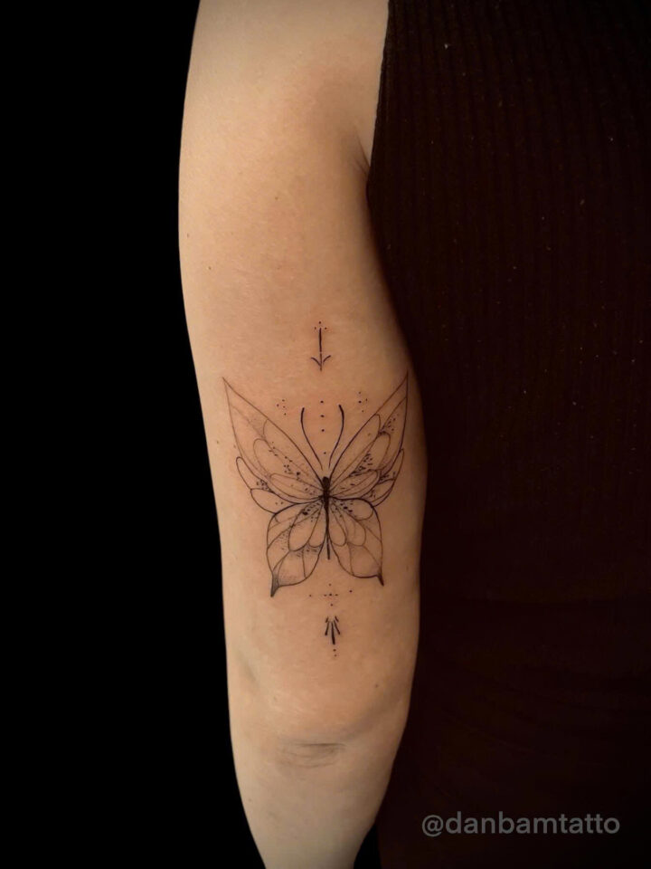 Fine line ornamental butterfly tattooed on the back of an upper arm