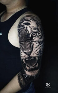 Stunning realistic black and grey tiger tattoo on shoulder and arm. Highly detailed roaring tiger with lifelike fur, eyes, and fangs. Professional tiger tattoo done at Dan Bam Tattoo Studio in Hoi An, Vietnam.