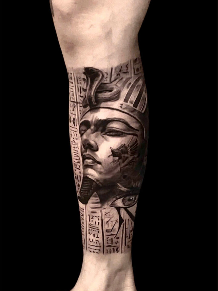 Black and grey realism tattoo of an Egyptian pharaoh and hieroglyphs on a calf