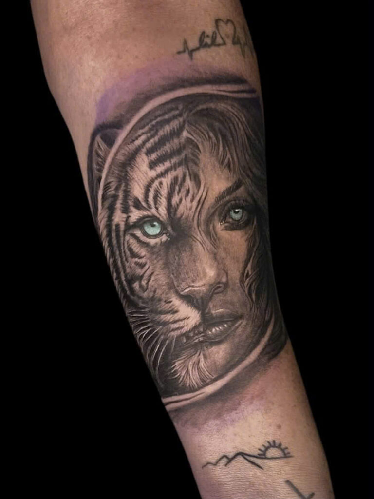 Realism tiger and woman portrait inside an astronaut helmet, tattooed on a forearm
