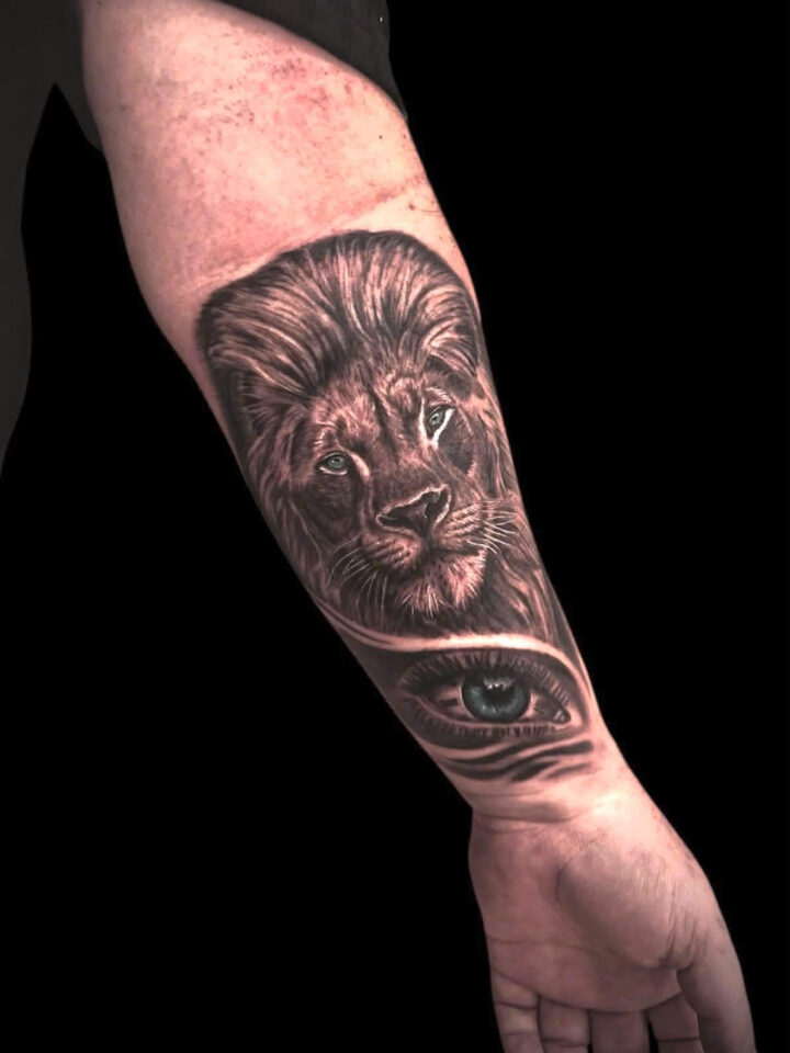Black and grey realism lion with an eye beneath it, tattooed on a forearm