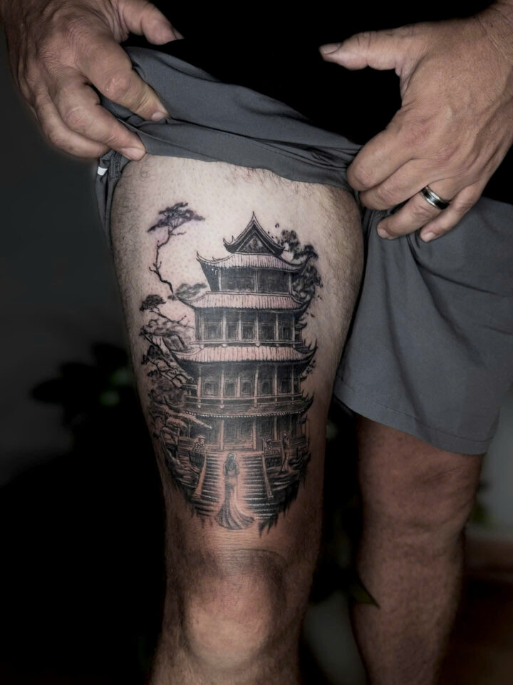 Black and grey realism tattoo of a Vietnamese pagoda and pine tree on a thigh