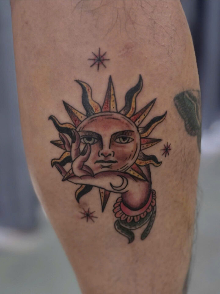 Traditional colour sun and moon face tattooed on a calf
