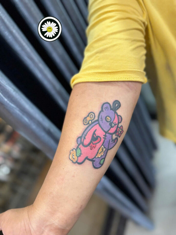 Colour cartoon creature tattooed in pink and purple on a forearm