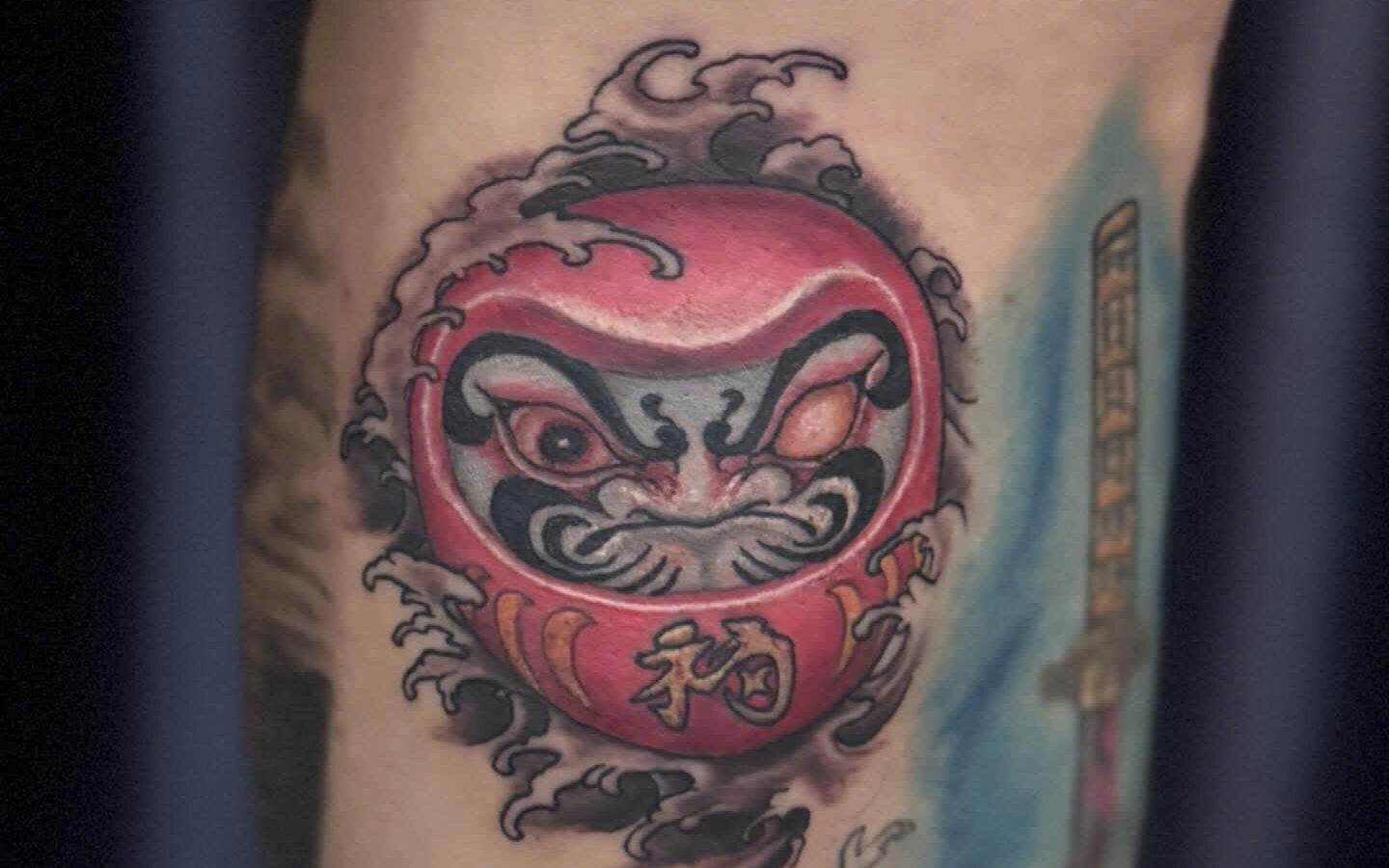 Colour daruma doll tattoo with wave detail on a calf