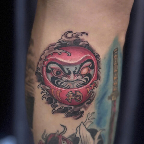 Colour daruma doll tattoo with wave detail on a calf
