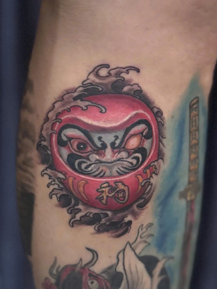 Colour daruma doll tattoo with wave detail on a calf