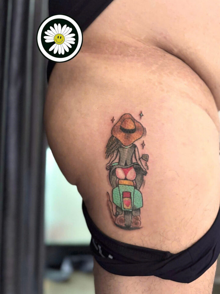 Colour tattoo of a woman riding a green scooter, on a thigh