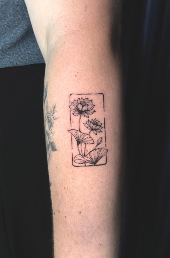 Fine line lotus flowers framed in a rectangle, tattooed on a forearm in Hoi An
