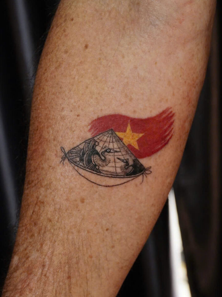 Non la conical hat tattooed over the red Vietnamese flag on a forearm