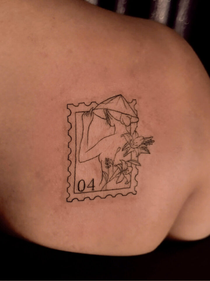 Postage stamp tattoo of a mountain landscape and wildflowers on a shoulder