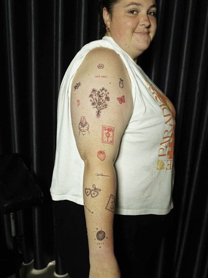 Arm covered in a collection of small fine line and red ink tattoos