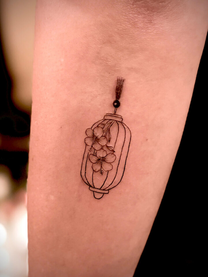 Fine line Hoi An lantern holding blossom flowers, tattooed on a forearm