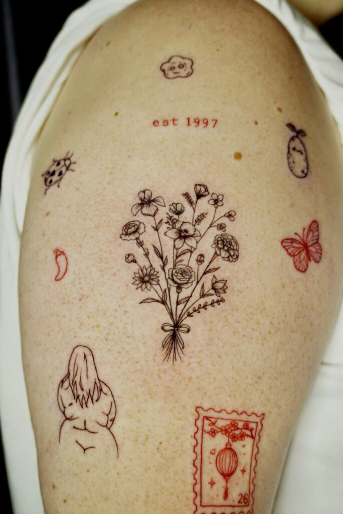 Wildflower bouquet tattoo with est 1997 lettering and small red minis on an upper arm